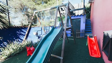 Children can play safely in this enclosed area with two slides and a climbing structure surrounded by lush greenery.