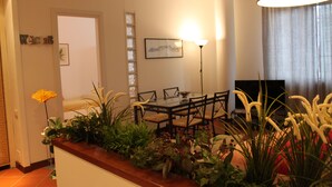 A dining area with a table, chairs, and a lamp. There is a plant on the table and a TV in the background. - 80m², Todo Reformado, Fibra Wifi, Estação Central, Metrô a Poucos Minutos (Milano)