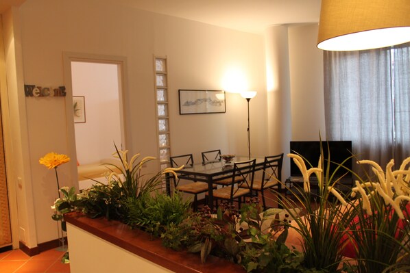A dining area with a table, chairs, and a lamp. There is a plant on the table and a TV in the background. - 80m², Todo Reformado, Fibra Wifi, Estação Central, Metrô a Poucos Minutos (Milano)