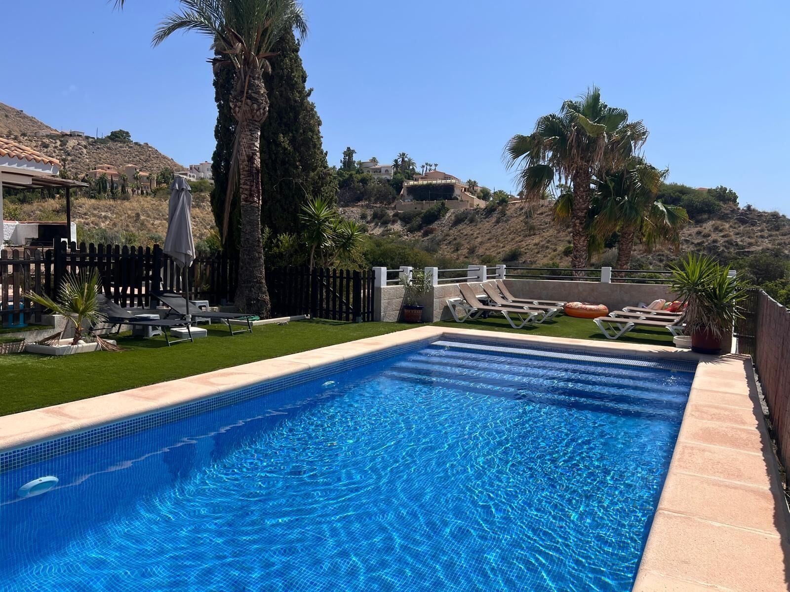 A rectangular swimming pool with clear blue water, surrounded by a wooden deck and palm trees.