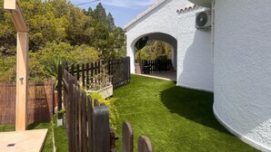 Un edificio blanco con un espacio exterior cubierto, una valla de madera y un césped bien cuidado.