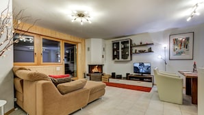 A modern living room with a sofa, TV, fireplace, and wooden paneling. - Appartement Matins St Laurent 1b - La Tzoumaz, 4 Vallees (La Tzoumaz)