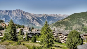 A mountain resort with multiple chalet-style buildings, surrounded by lush greenery and dramatic mountain peaks. - Appartement Matins St Laurent 1b - La Tzoumaz, 4 Vallees (La Tzoumaz)