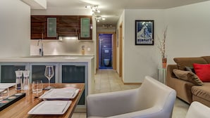 A modern kitchen with wooden cabinets, a dining area with a table set for four, and a living room with a sofa and a framed picture on the wall. - Appartement Matins St Laurent 1b - La Tzoumaz, 4 Vallees (La Tzoumaz)