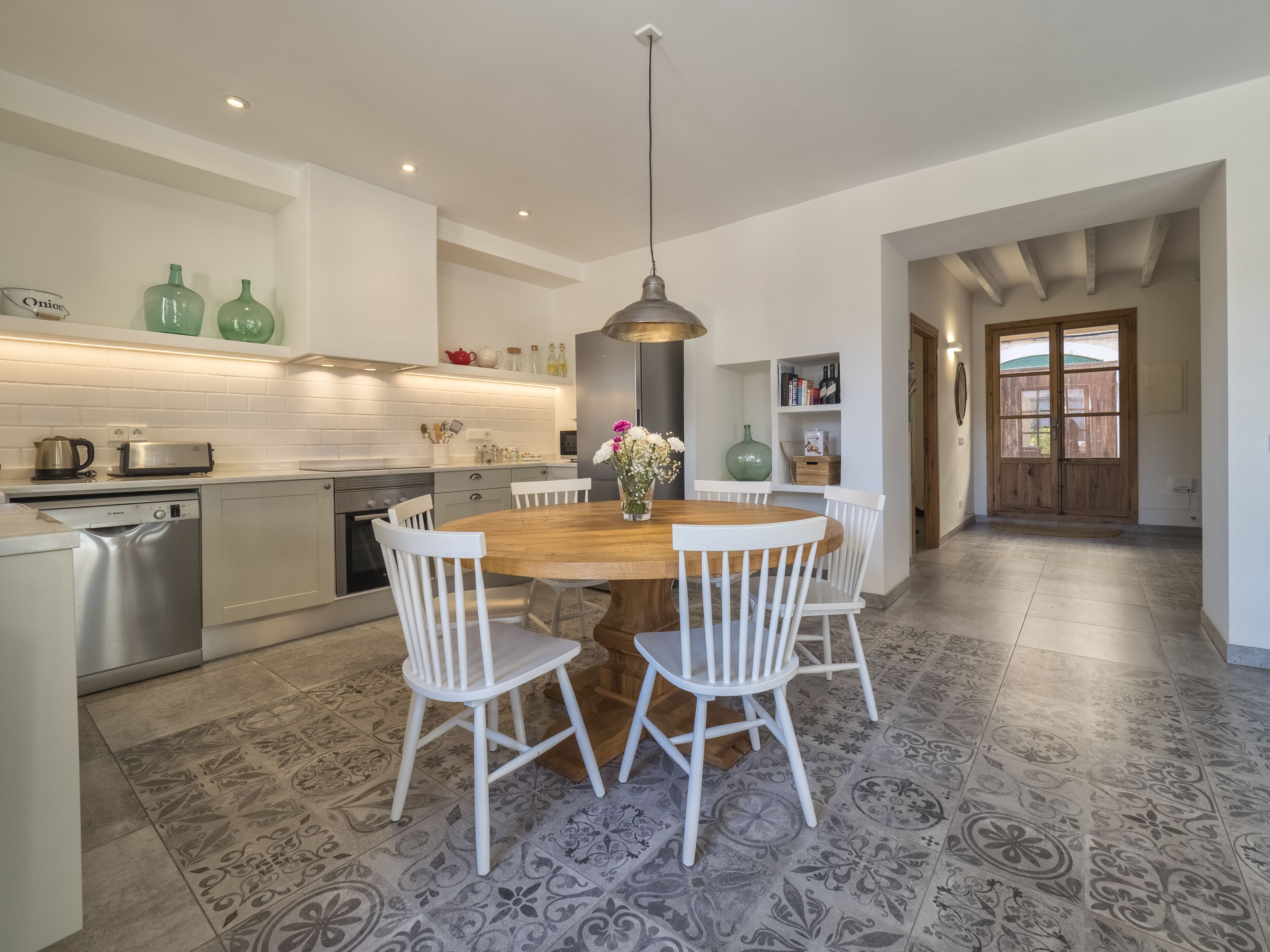 Una cocina moderna con armarios blancos, lavavajillas de acero inoxidable y una mesa de comedor de madera con sillas blancas.
