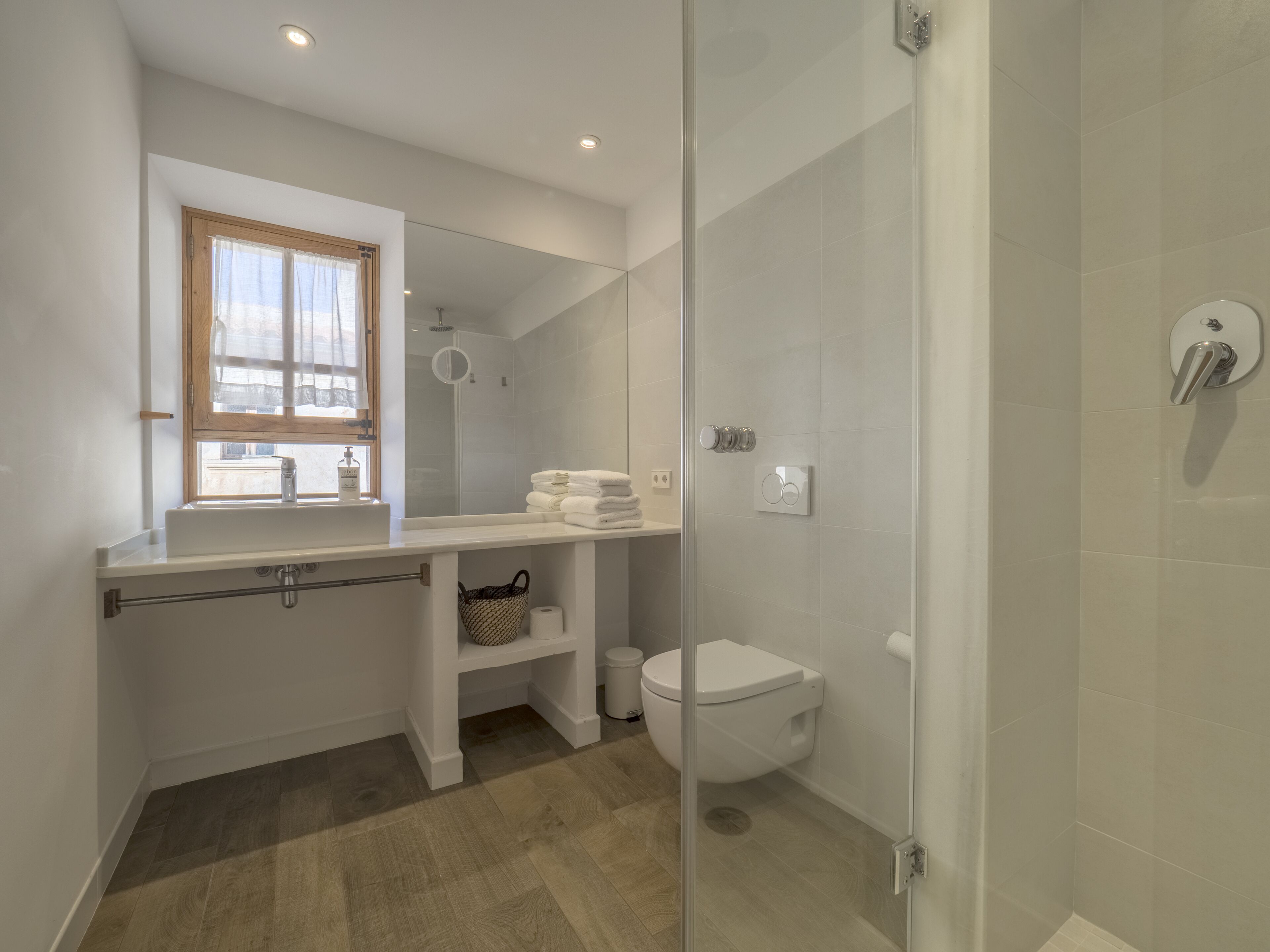 Een moderne badkamer met een douchecabine van glas, een toilet, een wastafel met spiegel en een raam met gordijnen.