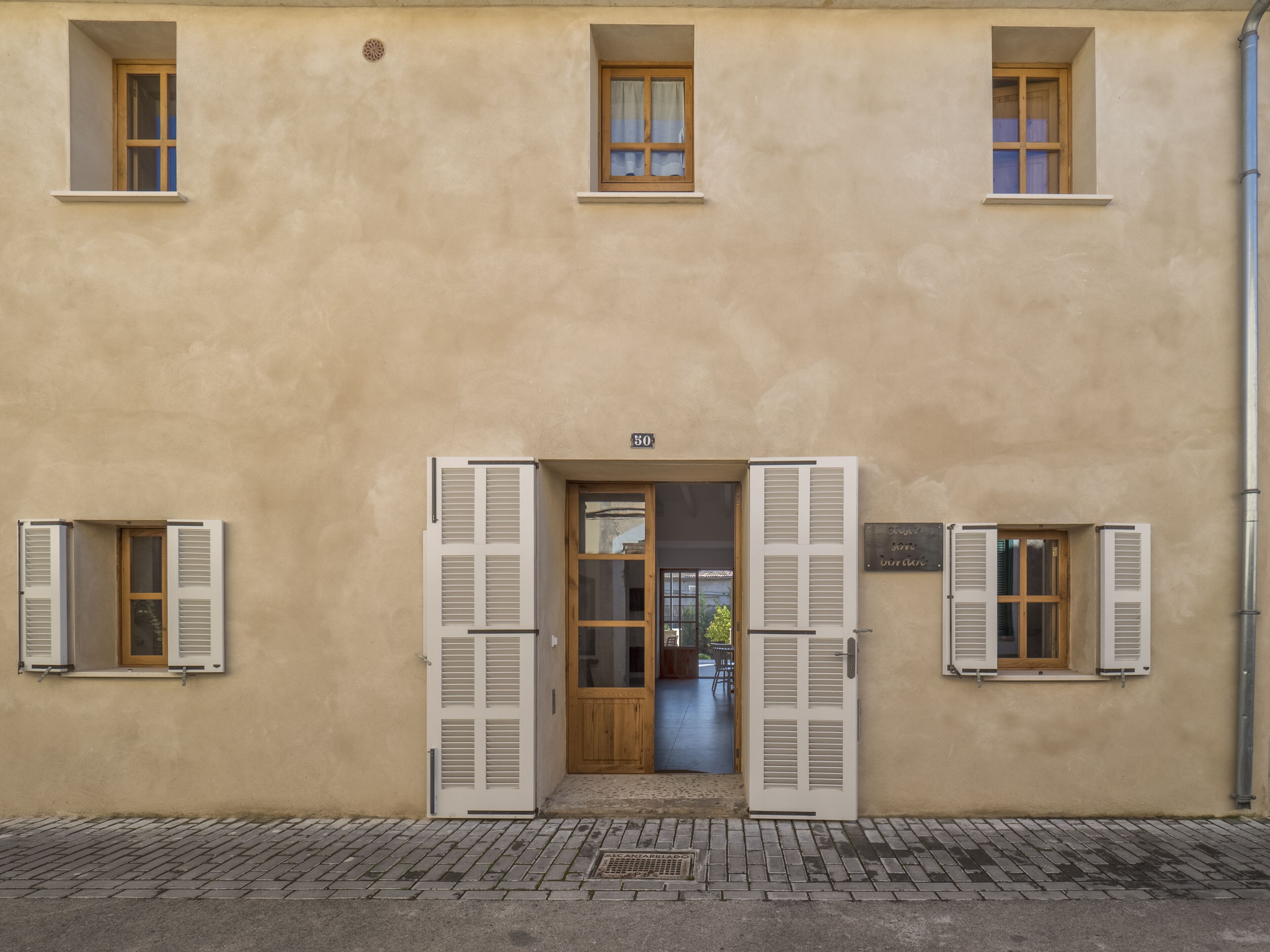 Un edificio de fachada color crema, una puerta de madera y contraventanas en las ventanas.