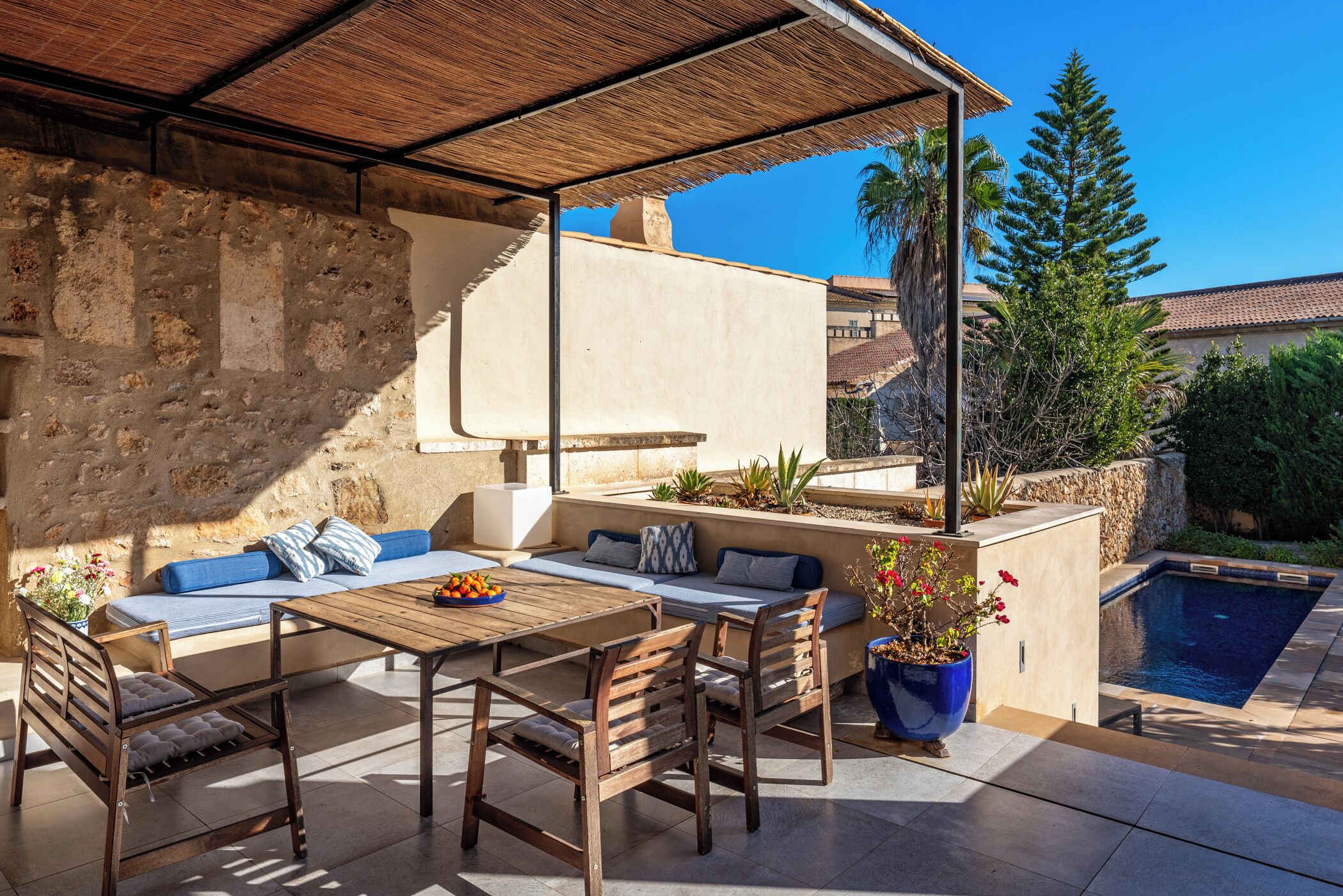 Un patio con una mesa de madera, sillas, un sofá y una planta en maceta.