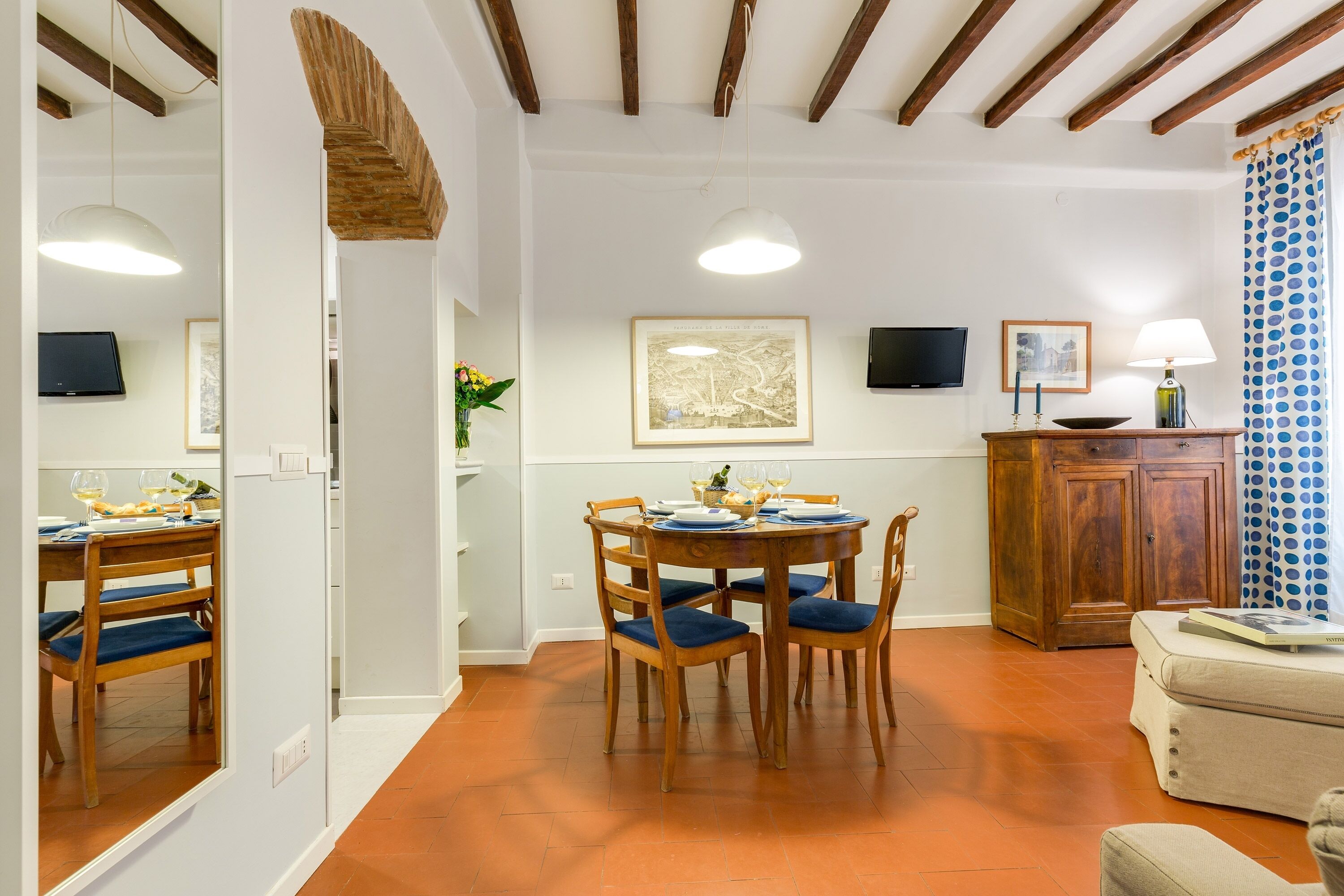 A dining area with a wooden table and chairs, a cabinet, and a television on the wall.