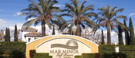 Skilt for Mar Menor Golf Resort omgivet af palmer og en velplejet græsplæne.