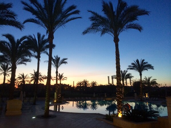 A pool area with palm trees and a sunset in the background. - Brand New Luxury Frontline Apartment With Golf, Pool & Lake Views (Torre Pacheco)