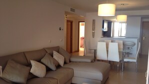Una sala de estar moderna con un sofá seccional, una mesa de centro de vidrio y un comedor con sillas blancas y una mesa de vidrio.
