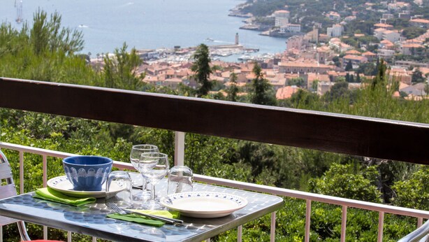 A table with a view of a coastal town, a blue bowl, and a white plate. - 3-star vacation rental. Large private balcony. Ocean View—Parking—Beach Access (Cassis)