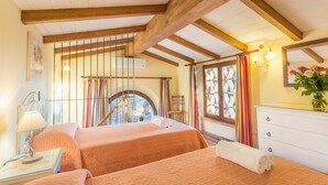 Un dormitorio con dos camas, vigas de madera, una ventana con cortinas, una mesita de noche con lámpara y un aparador.