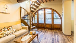 Un salón acogedor con una escalera de madera, un sofá con cojines estampados y una mesa de comedor con una bandeja de bebidas.