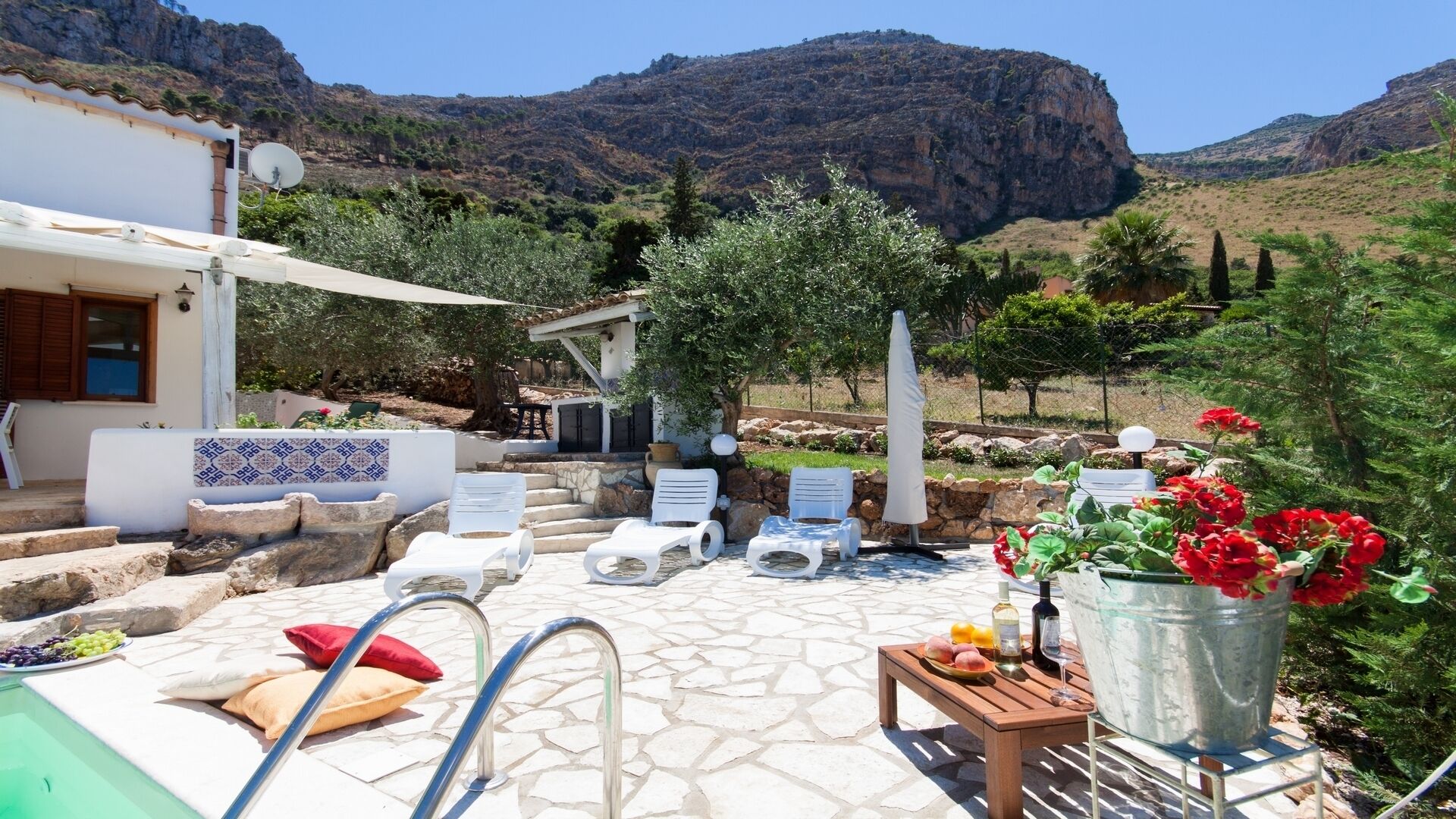 Zona de piscina con sillones de descanso, una mesa con bebidas y vistas a un paisaje montañoso.