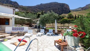 A poolside area with lounge chairs, a table with drinks, and a view of a mountainous landscape. -  Villa antico pozzo: pool, spa, sauna, sea view, 15 minutes from Scopello (Castellammare del Golfo)