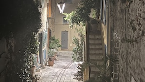 Une ruelle étroite pavée, bordée de bâtiments, avec le clocher d’une église en arrière-plan.