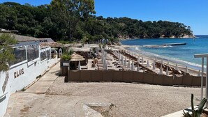 Un espace aménagé au bord de la plage, avec une terrasse en bois, des chaises longues, des parasols et une vue sur la mer.