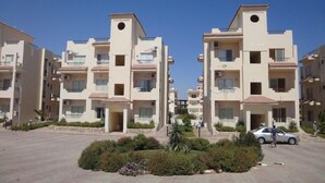 A residential building with multiple balconies, a central courtyard with plants, and a car parked in the driveway.