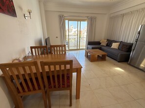 A living room with a dining table, sofa, and a view through the glass door.