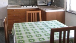 Une petite cuisine avec des meubles en bois, une cuisinière à gaz, un grille-pain et une table recouverte d’une nappe à motifs floraux verts.