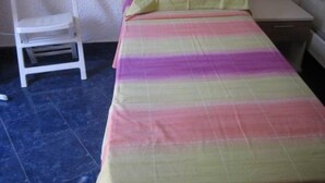 Une petite chambre avec un lit simple, une couette rayée aux couleurs vives, une chaise blanche et une table de chevet.