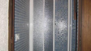 Une douche avec des portes en verre dépoli, des murs carrelés et un cadre de porte en bois.