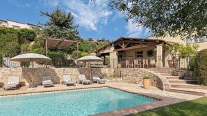 Ein Swimmingpool mit Liegestühlen und Sonnenschirmen, umgeben von Steinmauern und einer Steintreppe.