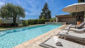 A swimming pool with lounge chairs and an umbrella, surrounded by stone walls and greenery.