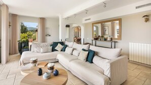 Ein Wohnzimmer mit Ecksofa, einem Couchtisch mit Dekoration, einem Kamin und Blick ins Freie.