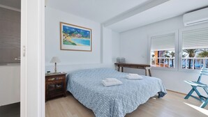 A bedroom with a bed, a nightstand, a window with blinds, a painting, and a view of the beach. - Flat in Benidorm Renovated Frontline with Terrace (Benidorm)