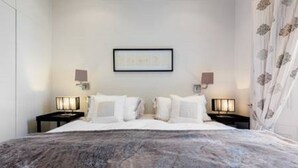 A hotel room with a large bed, two bedside tables with lamps, a framed picture on the wall, and a window with curtains.