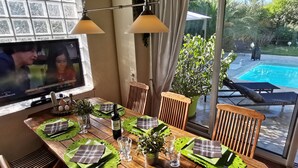 Uma sala de jantar com uma mesa de madeira posta para quatro pessoas, com jogos americanos xadrez e talheres verdes. Há uma garrafa de vinho e copos sobre a mesa.