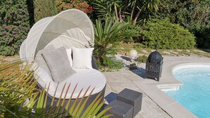 Uma área de estar coberta ao ar livre, com almofadas e vista para a piscina.