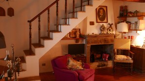Un salon chaleureux avec un escalier en bois, une cheminée, un fauteuil rouge et une chaise en bois.