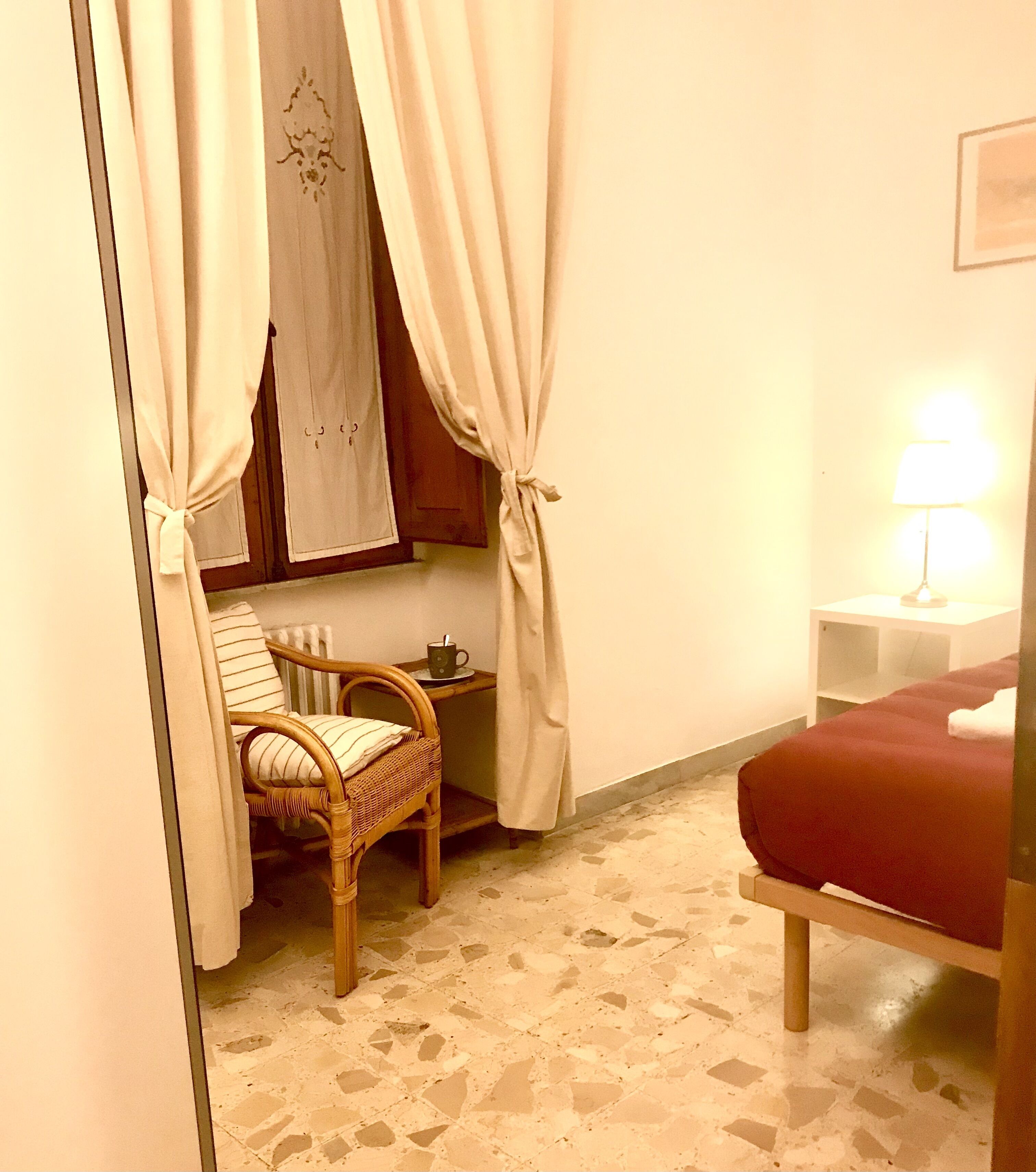 A room with a bed, a chair, a small table with a cup, and a lamp.