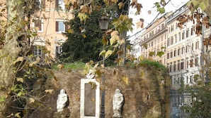 A stone wall with two statues, a metal lamp post, and a wrought iron gate.