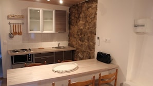 Une cuisine compacte avec un mur d’accent en pierre, des armoires en bois, un four à micro-ondes et une table à manger avec des chaises.