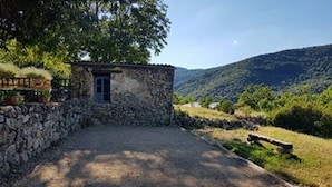 Un bâtiment en pierre avec une petite porte, entouré d’une allée gravillonnée et d’un mur de pierre.