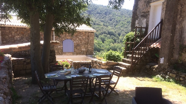 Un bâtiment en pierre doté d’un espace de restauration extérieur rustique, avec une table dressée pour quatre personnes, entouré de murs en pierre et d’un escalier menant à un niveau supérieur.