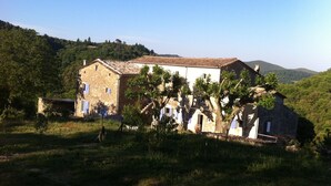 Un bâtiment rustique en pierre, doté d’un toit en tuiles, entouré d’une végétation luxuriante et d’arbres.