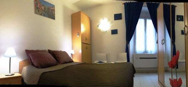 A hotel room with a bed, bedside lamps, a wardrobe, a mirror, and a window with curtains.
