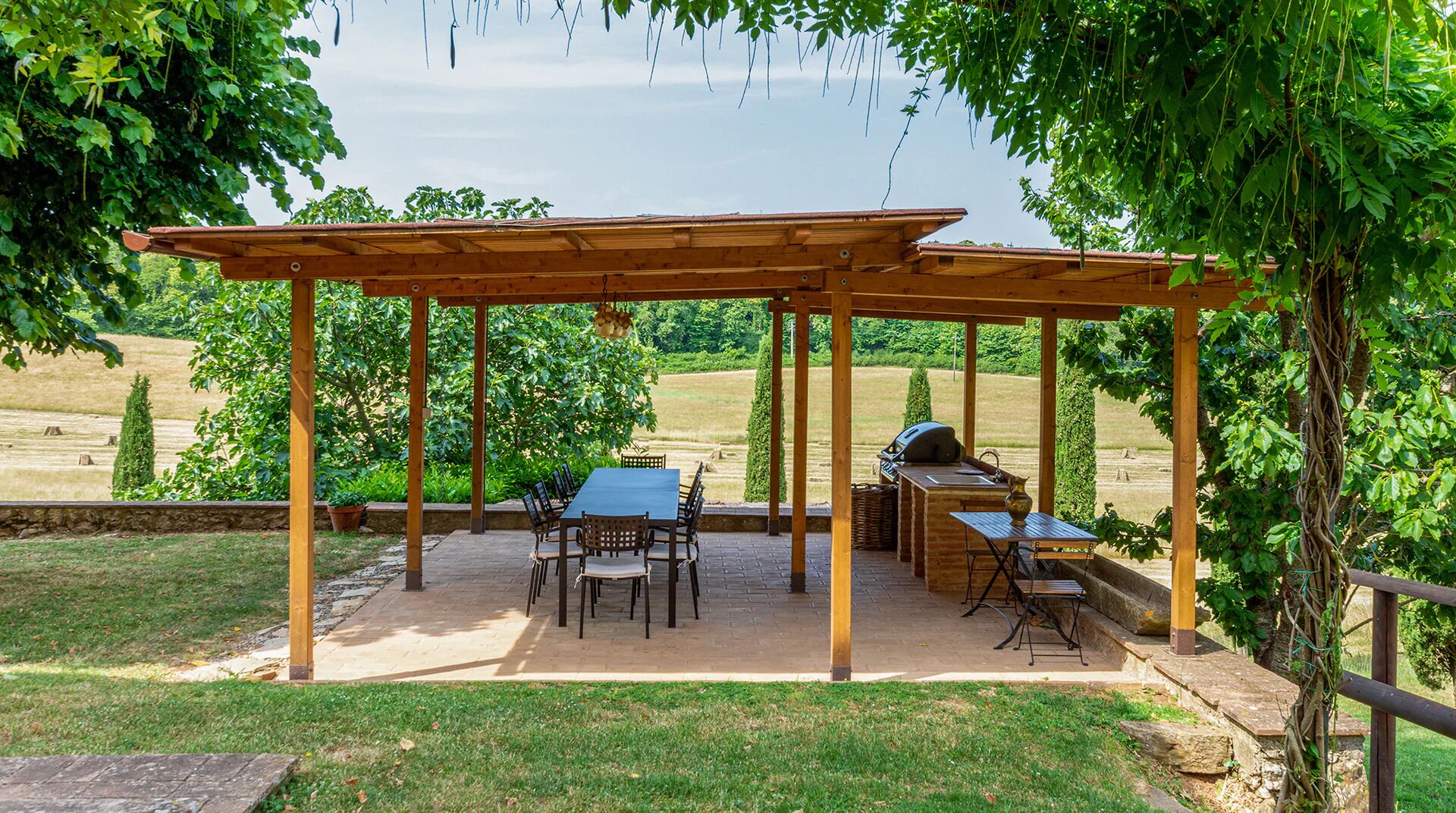 Een terras buiten met een pergola, een barbecue en een tafel met stoelen.