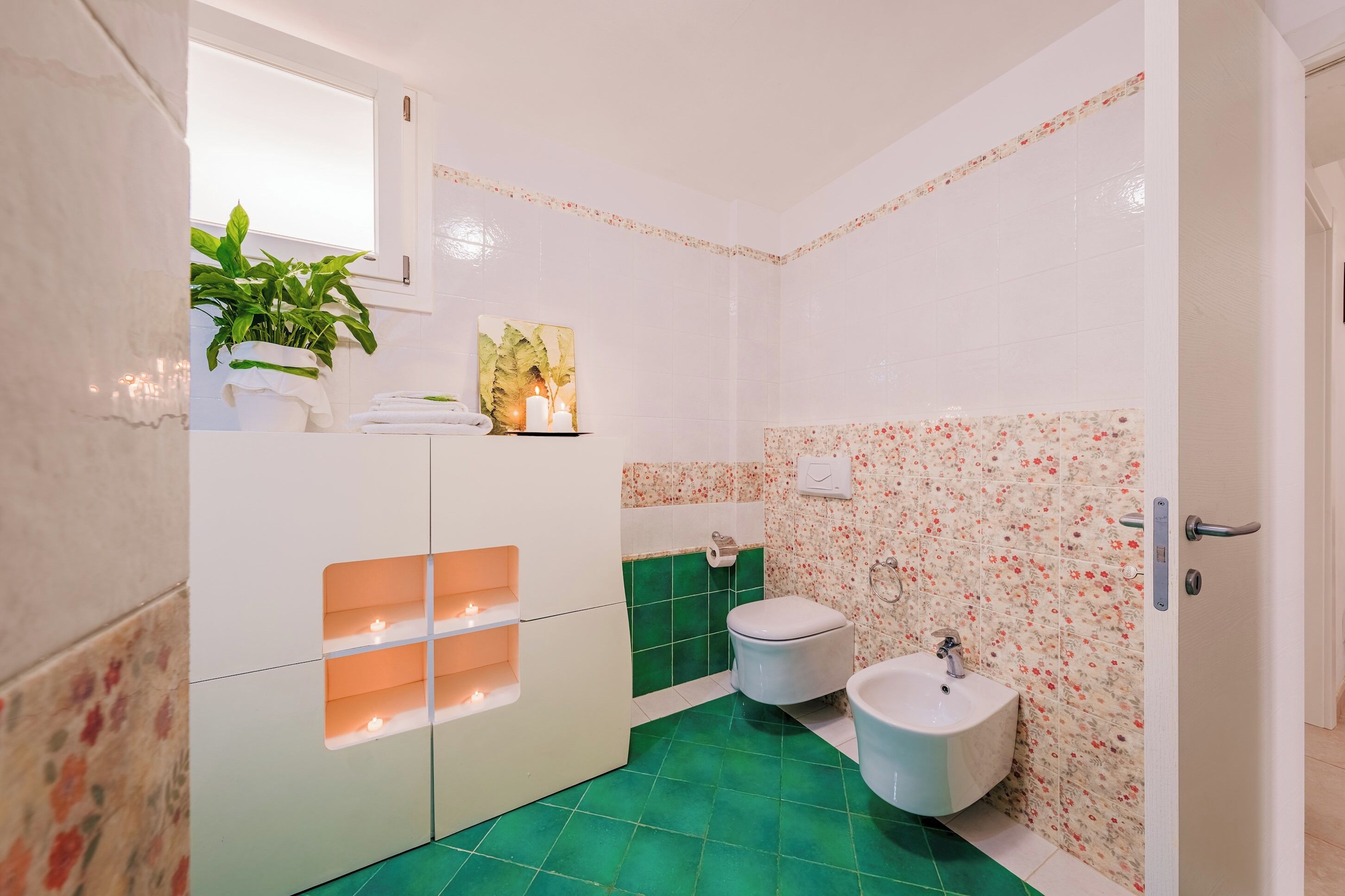 A bathroom with a green floor, white walls, a toilet, a sink, and a plant.