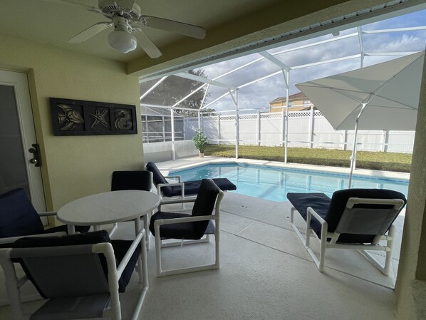 A covered patio with a pool, white chairs, a table, and a ceiling fan. - 15 min from Disney, private pool in secure gated community (Davenport)