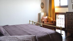 Une chambre à coucher avec un lit, une chaise, une commode et une fenêtre avec des rideaux.