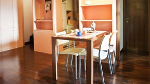 Un coin repas avec une table et des chaises, un espace cuisine avec des placards et une cuisinière, et une porte en bois.