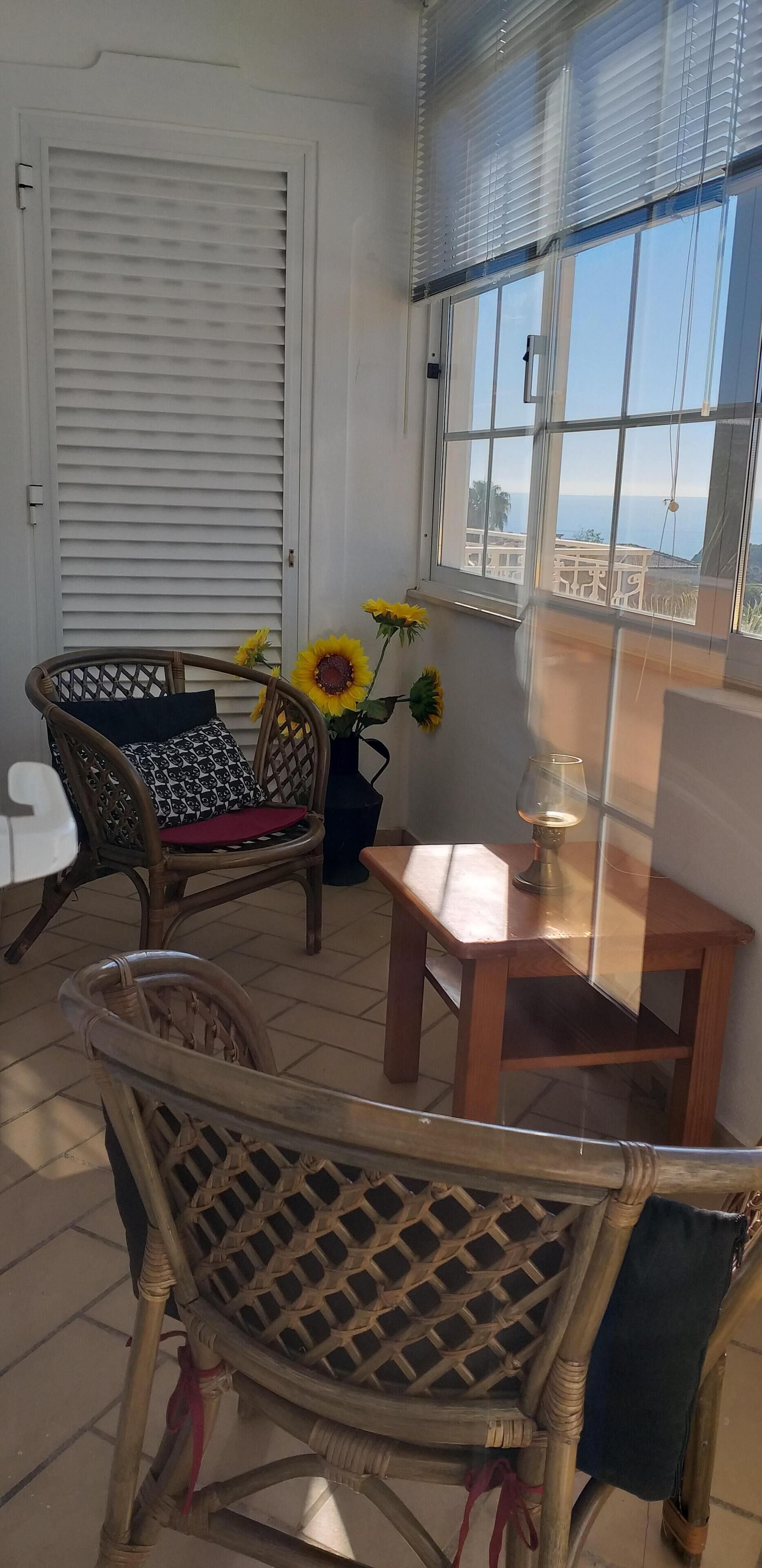 Ein Zimmer mit Korbmöbeln, einem Fenster mit Jalousien und Meerblick.