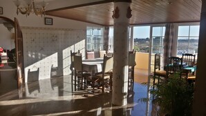 A spacious room with a high ceiling, large windows offering a view of the landscape, and a dining area with wooden furniture. - Villa with private pool, terrace and sea views (Albufeira)